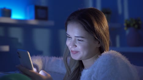 Happy-young-woman-texting-on-phone-at-night-at-home.